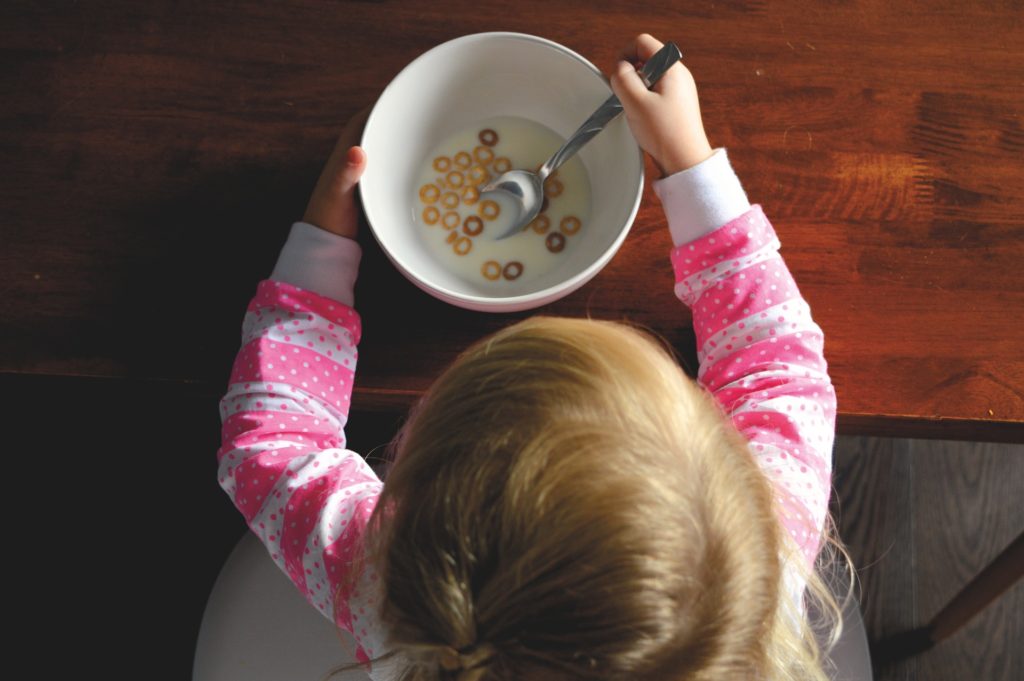 View from above of a toddler eating a bowl of cereal.
